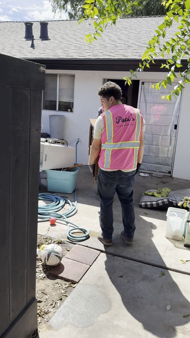 Papi’s crew in pink vests carrying a dresser out through a side-yard gate near Clovis