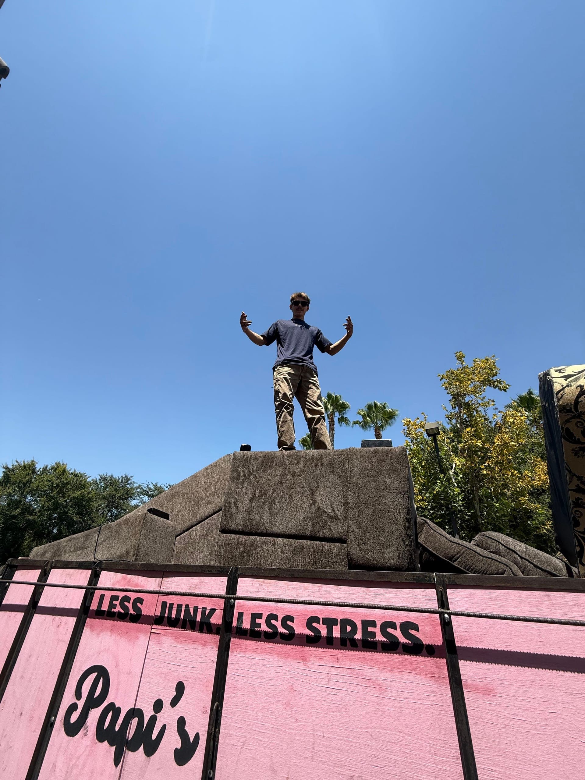 Papi's crew member standing on top of a fully loaded pink 'Less Junk. Less Stress.' trailer in Clovis