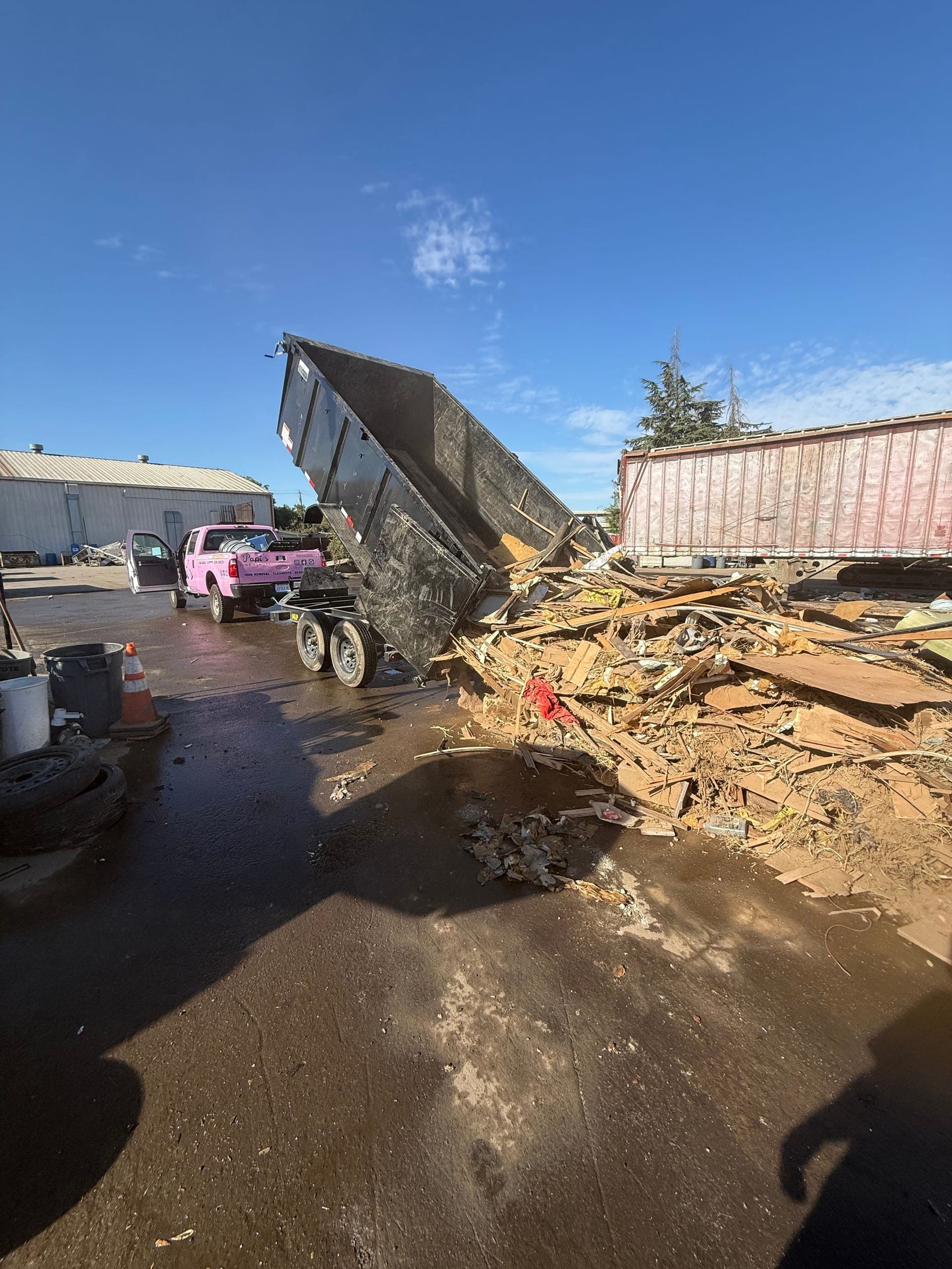 Papi's dump trailer tipping a load of debris at a Fresno disposal yard, pink truck alongside