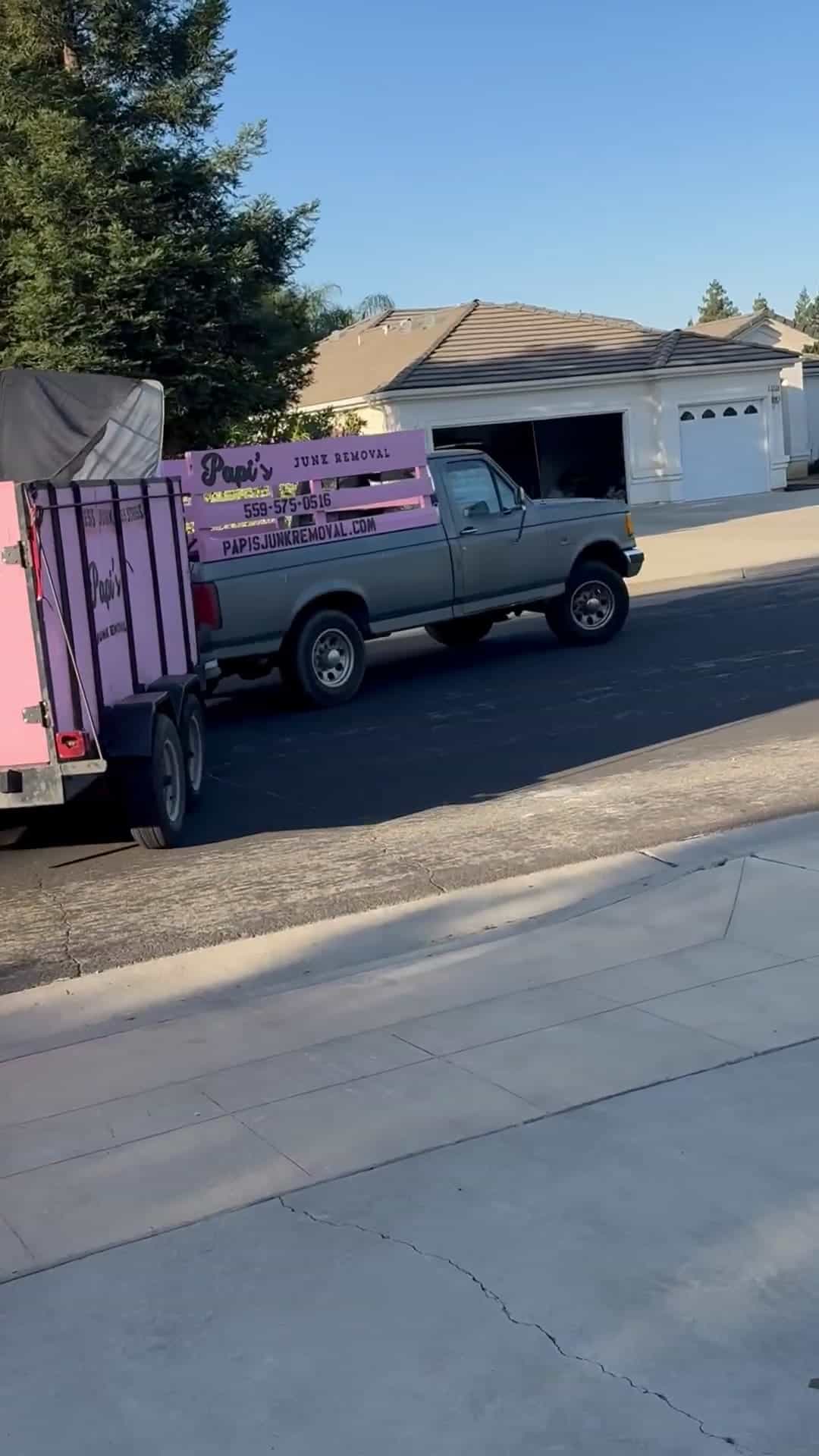 Papi's Junk Removal pickup towing the pink trailer down a Clovis neighborhood street